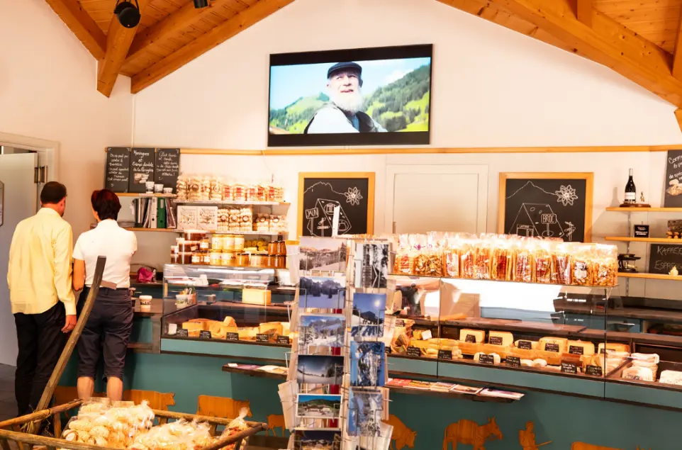 Affichage dynamique dans la fromagerie Jaun-Bellegarde : un outil puissant pour valoriser les produits artisanaux Écran professionnel d’affichage dynamique dans la fromagerie de montagne Jaun-Bellegarde, diffusant du contenu au-dessus du comptoir