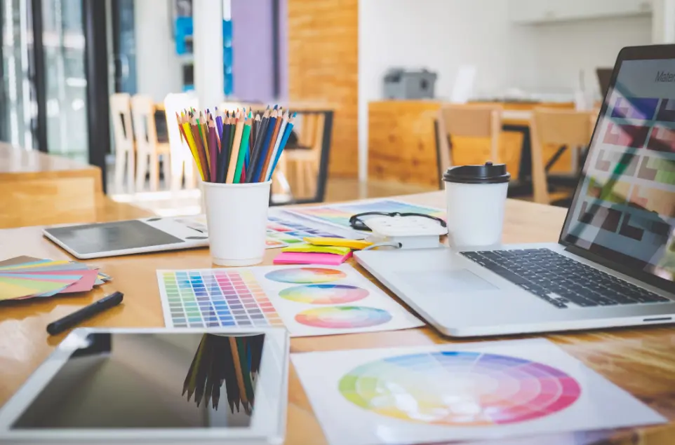 Création de contenus visuels sur mesure avec Hubgrade – processus collaboratif et formats adaptés Bureau créatif avec ordinateur portable, tablette, nuanciers et crayons de couleur pour la conception de contenus visuels Hubgrade